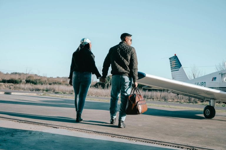 Couple marchant vers un avion sur un tarmac, bagage en main, ciel bleu