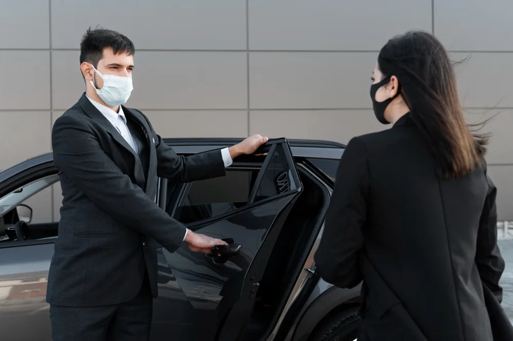 Chauffeur masqué ouvre la porte d’une berline à une passagère