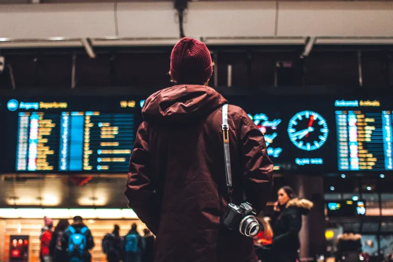 Passager de dos regardant les départs, caméra en bandoulière